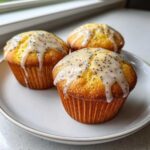 Three golden baked lemon poppy seed muffins topped with a thick, dripping lemon glaze and visible poppy seeds.
