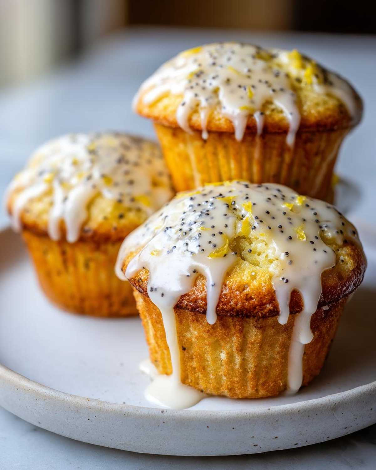 Three golden lemon poppy seed muffins topped with thick, dripping lemon glaze and poppy seeds.