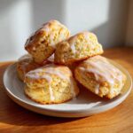 A stack of freshly baked, golden lemon scones topped with a thick, dripping lemon glaze.