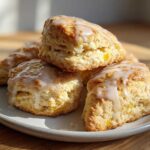 Close-up of several fluffy lemon scones topped with a sweet white glaze, stacked on a light-colored plate.