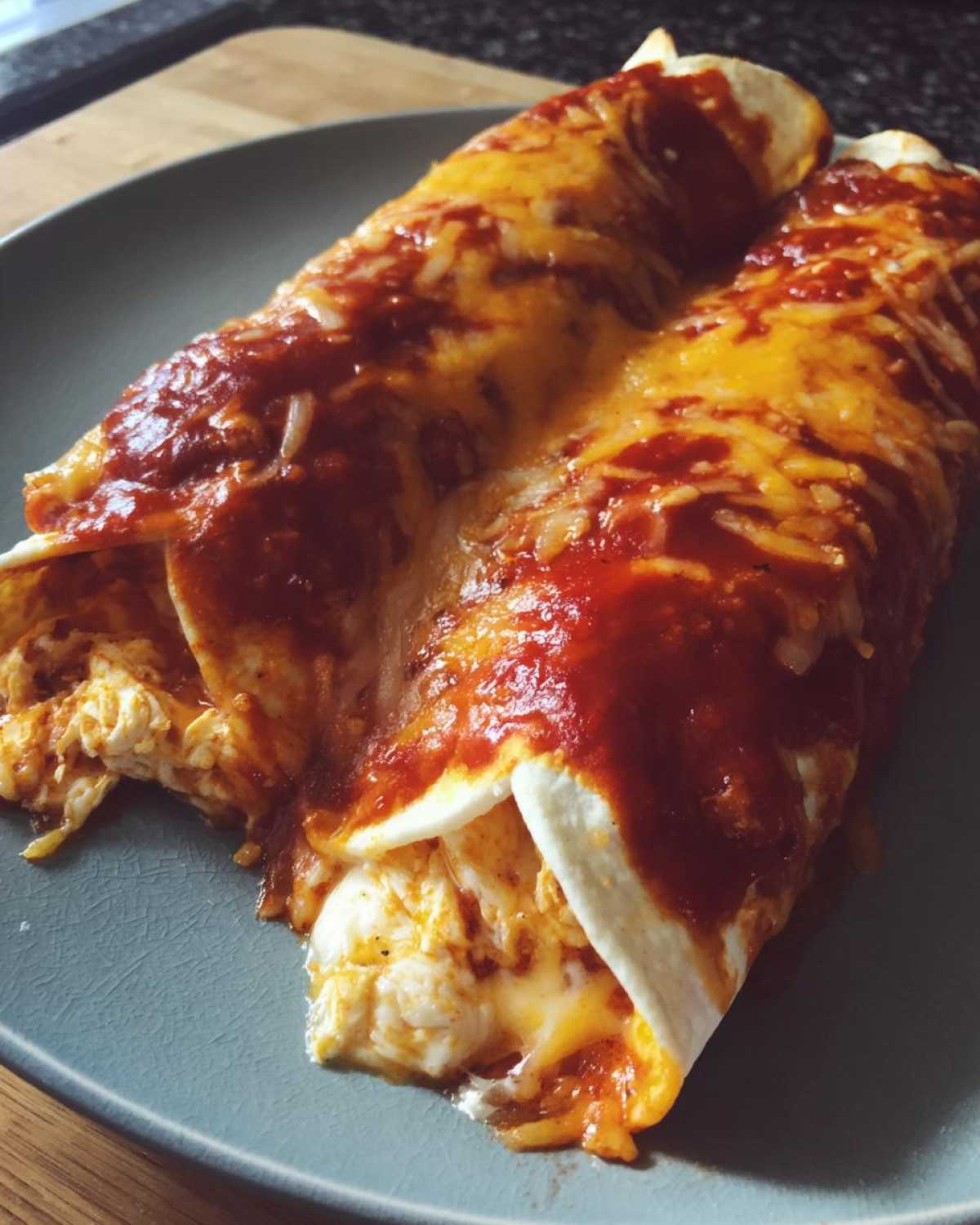 Two rolled cheese enchiladas covered in melted cheddar and red enchilada sauce on a blue plate.