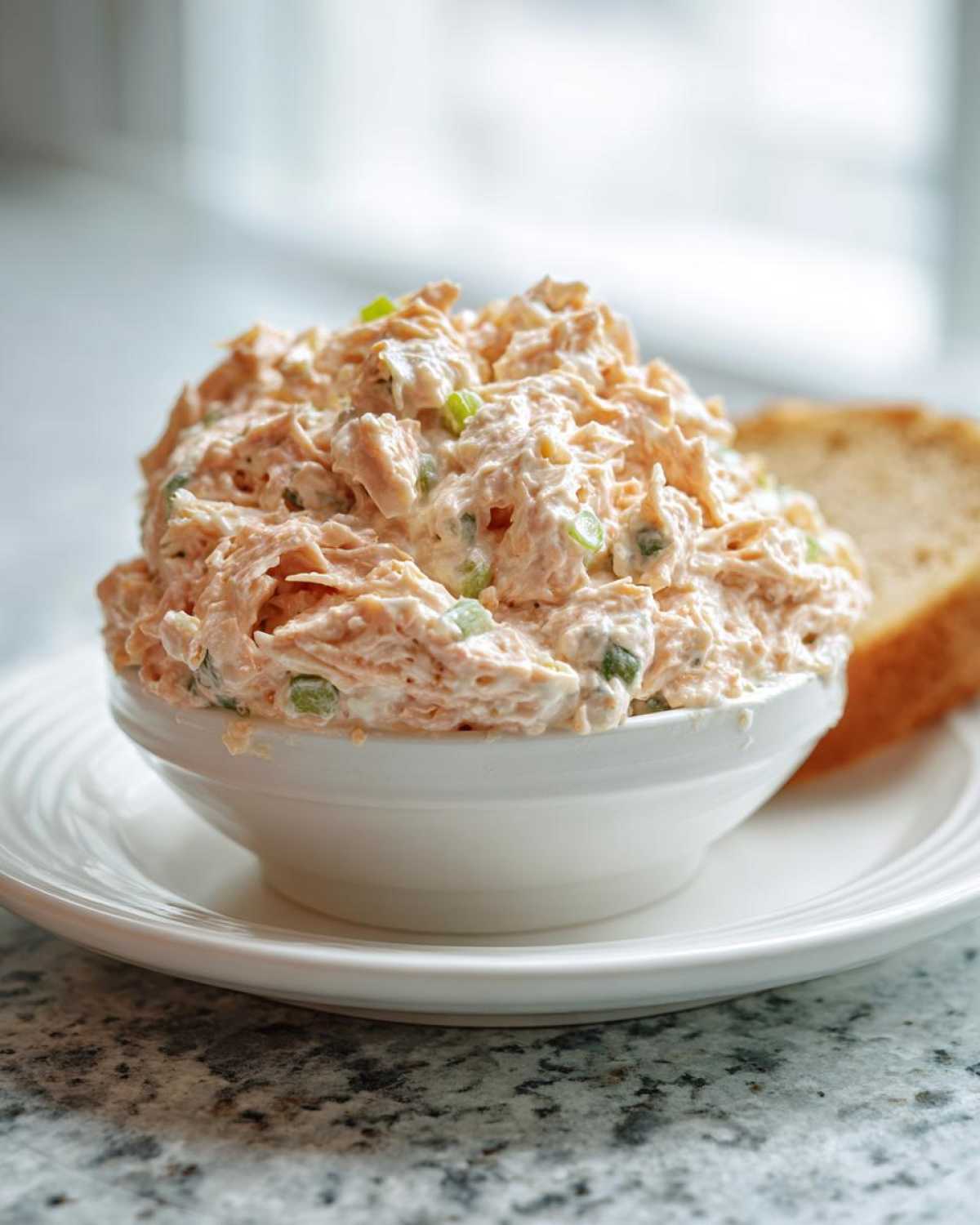 A white bowl filled high with creamy, shredded ham salad recipe mixed with green onions, served on a white plate.