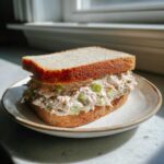 A thick sandwich filled with creamy ham salad recipe mixture and celery chunks, served on toasted white bread.