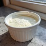A small white ramekin filled with creamy homemade garlic sauce, topped with a sprinkle of white powder.