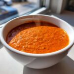 Close-up of steaming, bright orange chili cheese dip in a white bowl near a window.