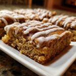 Close-up of several moist snickerdoodle blondies squares drizzled with white vanilla icing on a white platter.