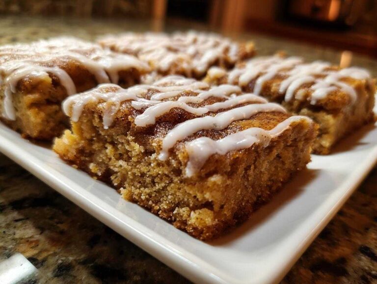 Close-up of several moist snickerdoodle blondies squares drizzled with white vanilla icing on a white platter.