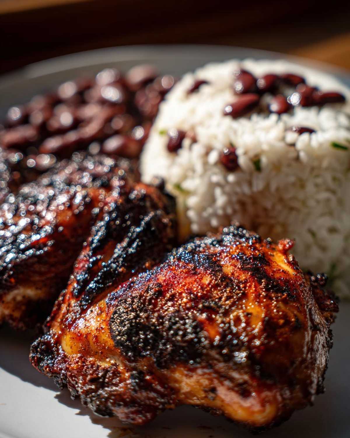 Close-up of two pieces of perfectly charred Jamaican jerk chicken served with rice and peas.