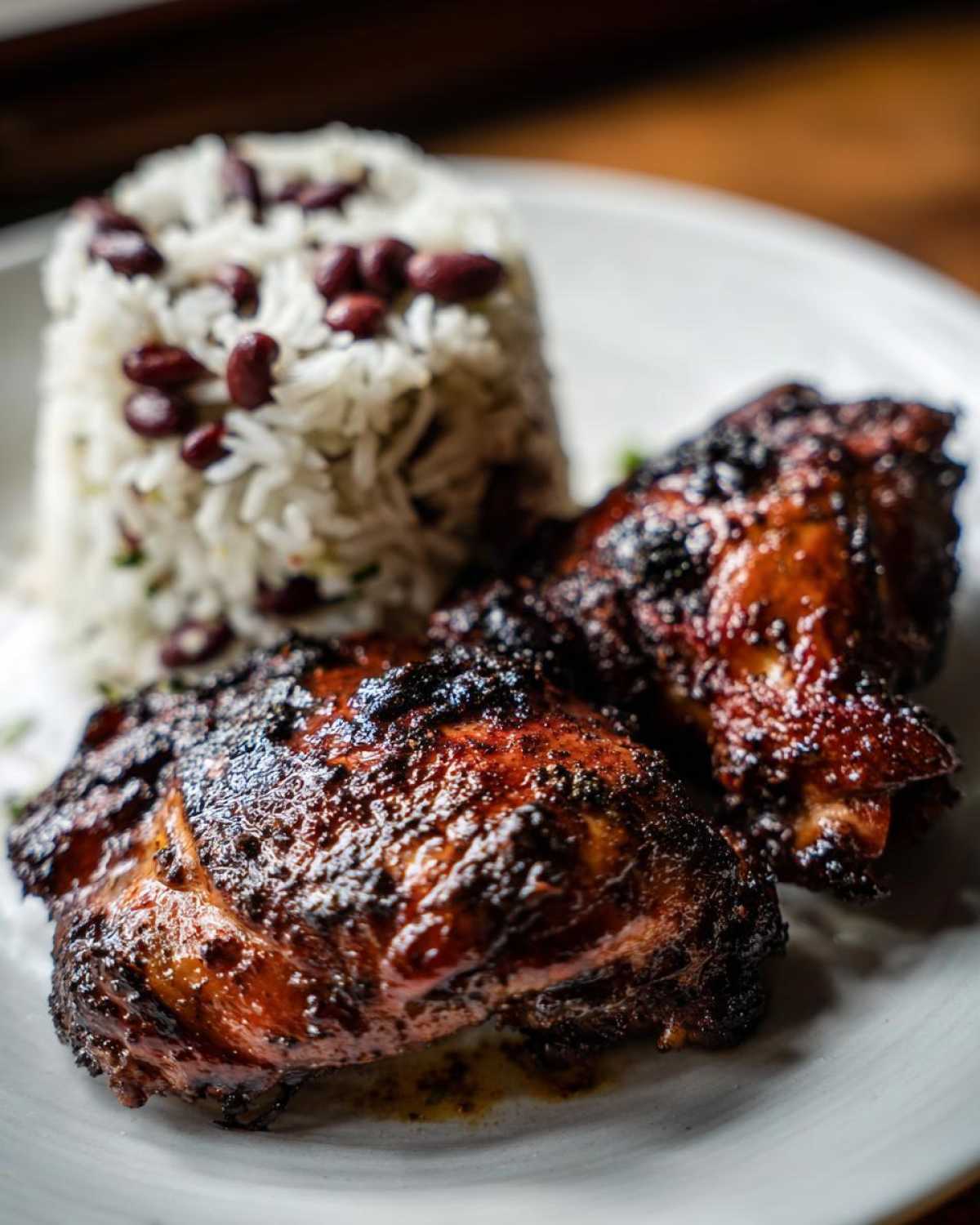 Two pieces of dark, glazed Jamaican jerk chicken served with a mound of rice and peas.