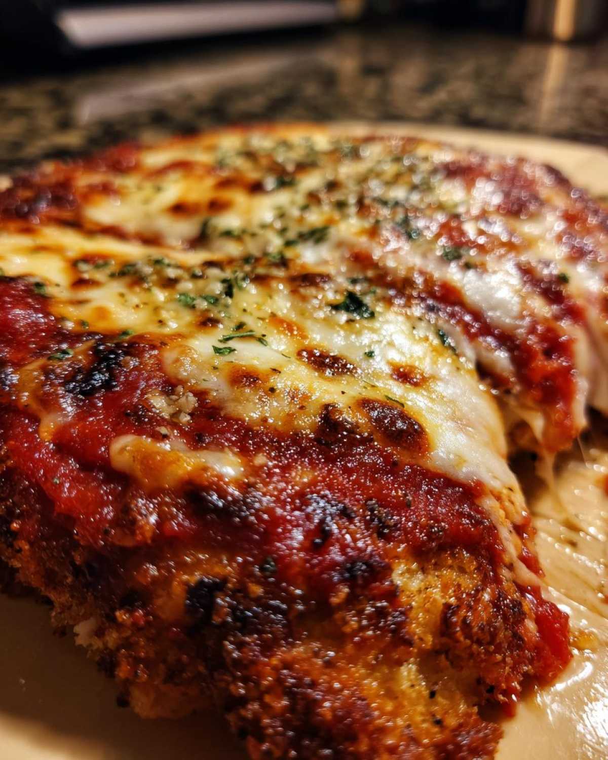 Close-up of a piece of keto chicken parmesan covered in melted mozzarella cheese, rich tomato sauce, and herbs.
