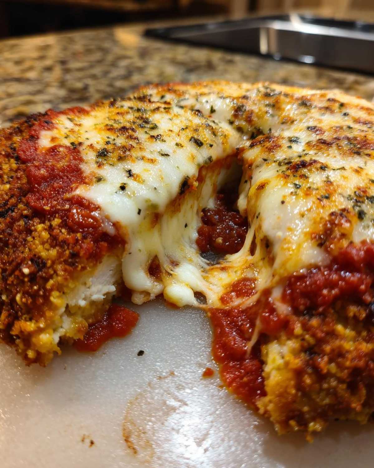 Close-up of keto chicken parmesan with a piece removed, showing melted mozzarella cheese stretching between the halves.
