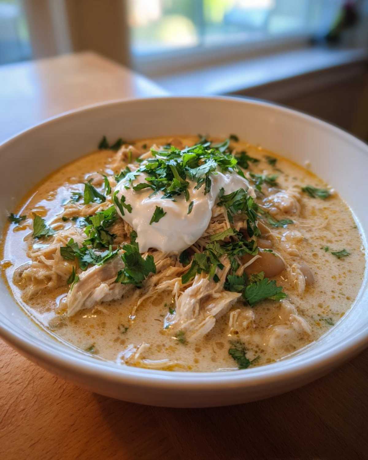 A white bowl filled with creamy keto white chicken chili, topped with shredded chicken, sour cream, and fresh cilantro.