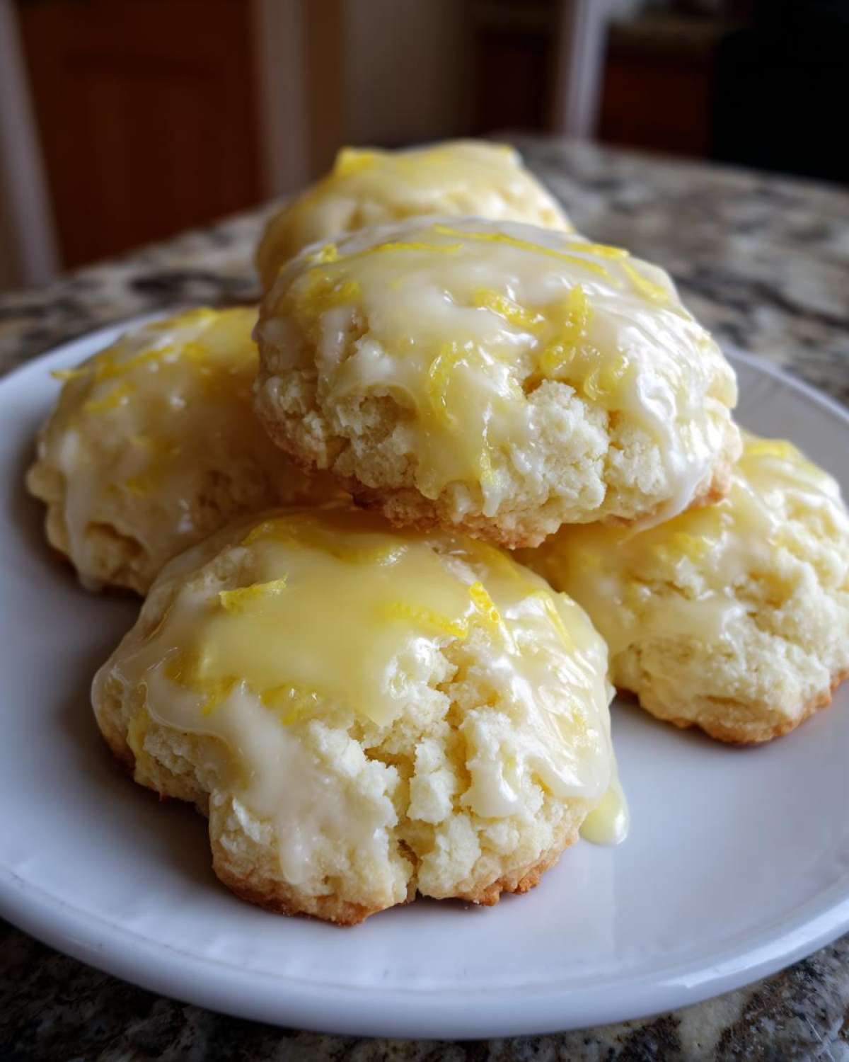 A stack of soft, glazed lemon ricotta cookies topped with bright yellow zest on a white plate.