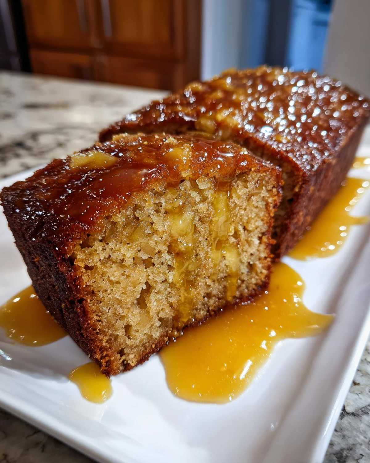 A close-up of a slice of moist apple dapple cake, topped with a shiny caramel glaze and served with extra sauce.