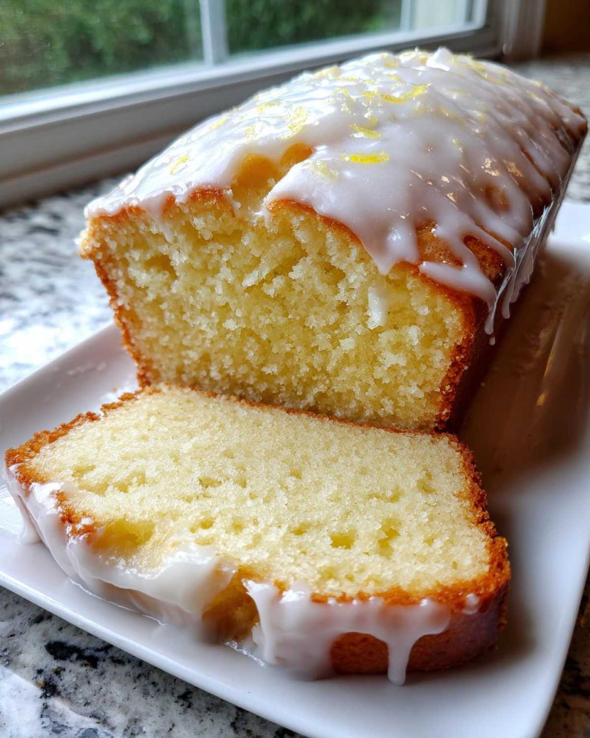 Close-up of a moist lemon loaf, sliced, showing the crumb texture and thick white lemon glaze.