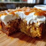 Close-up of a moist slice of pumpkin poke cake topped with white frosting and drizzled heavily with caramel sauce.