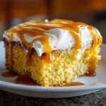 A close-up of a moist slice of pumpkin poke cake topped with white frosting and dripping caramel sauce.