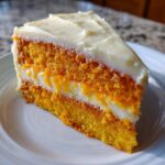 Close-up of a moist slice of Creamsicle Cake featuring bright orange layers and white cream filling and frosting.
