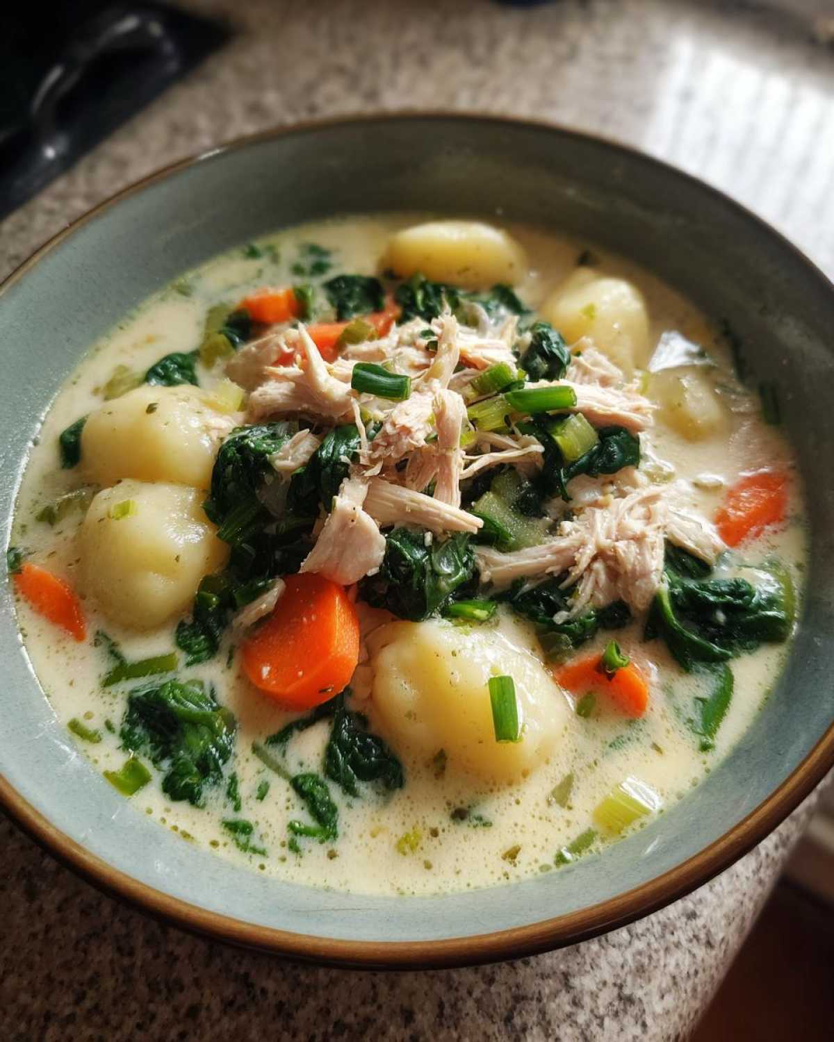 A close-up of a bowl of creamy olive garden chicken gnocchi soup, topped with shredded chicken, spinach, and carrots.