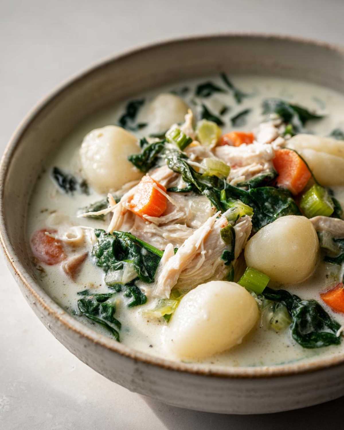 Close-up of a bowl of creamy Olive Garden Chicken Gnocchi Soup with shredded chicken, spinach, carrots, and gnocchi.