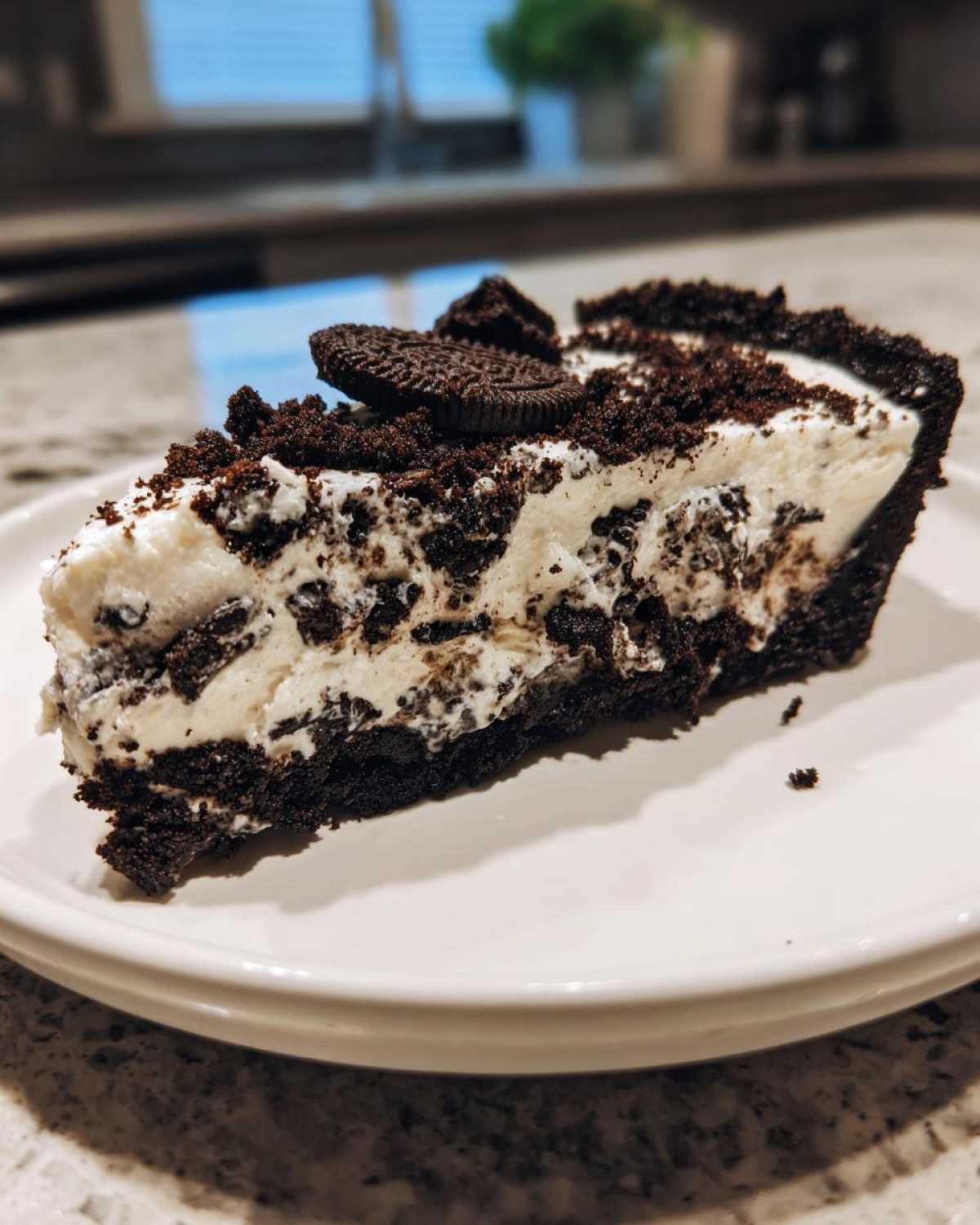 A close-up slice of creamy Oreo pie with a dark chocolate crust and cookie crumbles on top.
