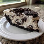 A rich slice of no-bake Oreo pie with a dark crust and creamy filling topped with crushed cookies.