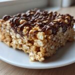 A close-up of a thick peanut butter rice krispie treats square topped with a dark chocolate drizzle.