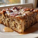 A moist slice of pecan pie bread pudding topped with pecans and dripping with caramel glaze.