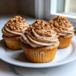 Three freshly baked pecan pie cupcakes topped with cinnamon-swirled frosting and chopped pecans.