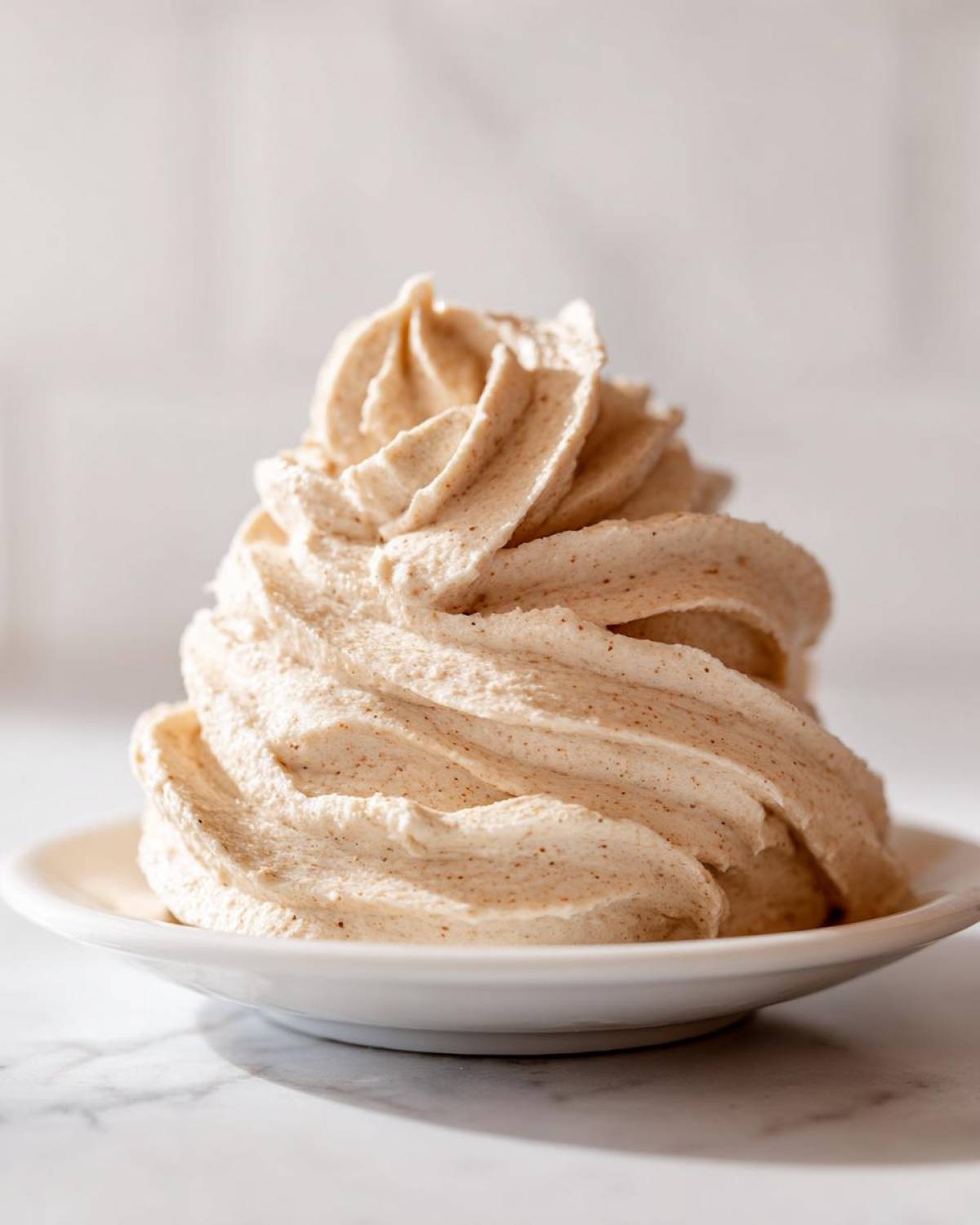 A tall swirl of fluffy, light brown cinnamon butter piped onto a small white dish.