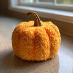 A beautifully shaped pumpkin cheese ball coated in orange crumbs, sitting on a countertop near a window.