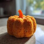 A close-up, low-angle shot of a textured, orange pumpkin cheese ball sitting on a countertop.