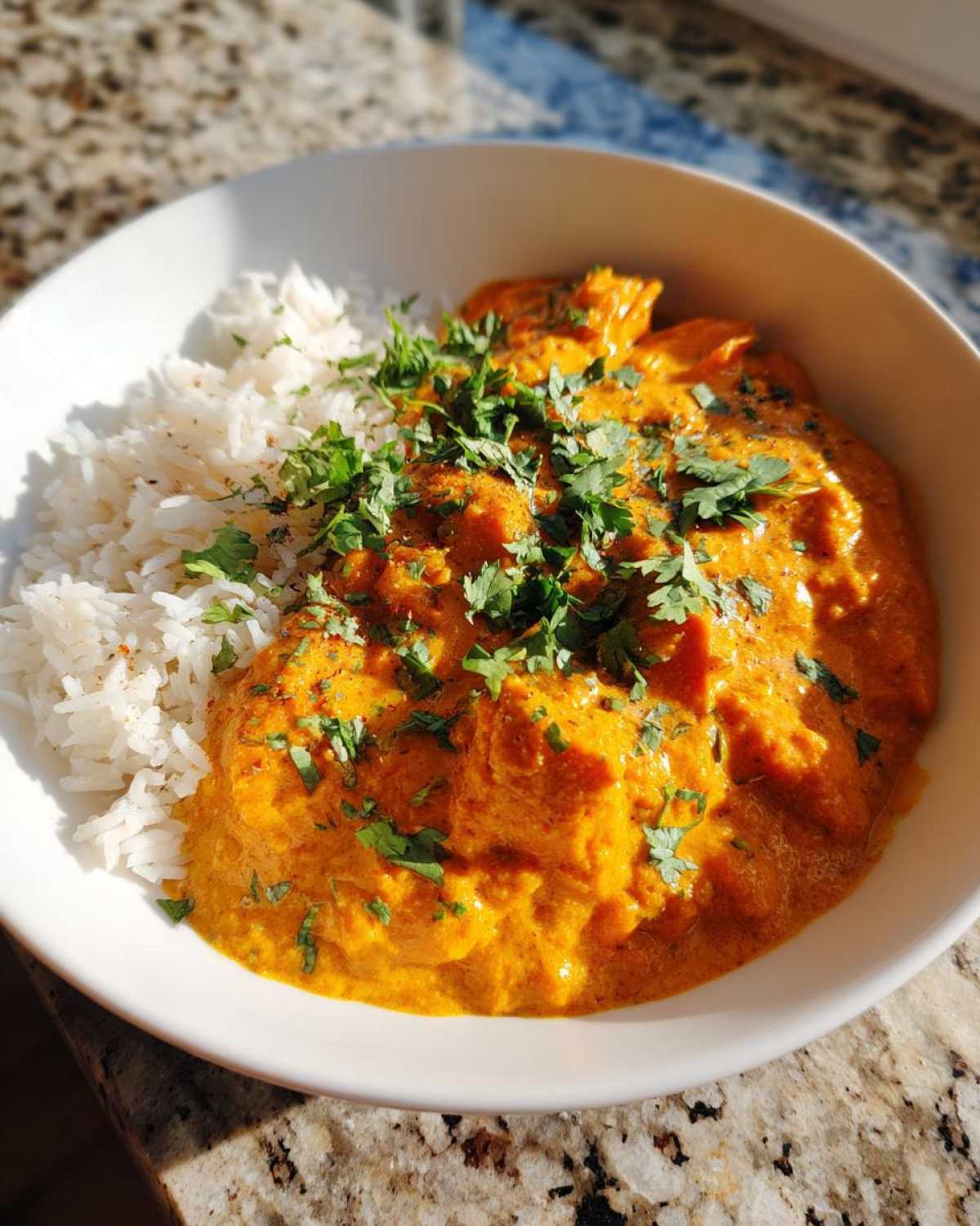 A white bowl filled with rich orange pumpkin curry served alongside fluffy white rice, garnished with fresh cilantro.