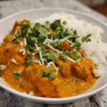 A white bowl filled with rich orange pumpkin curry served alongside fluffy white rice, garnished with cilantro.