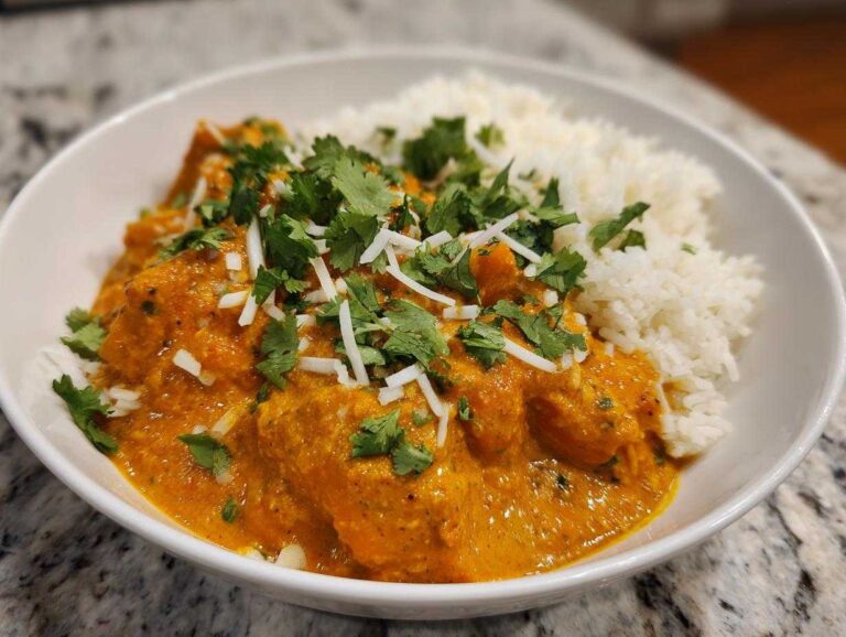 A white bowl filled with rich orange pumpkin curry served alongside fluffy white rice, garnished with cilantro.