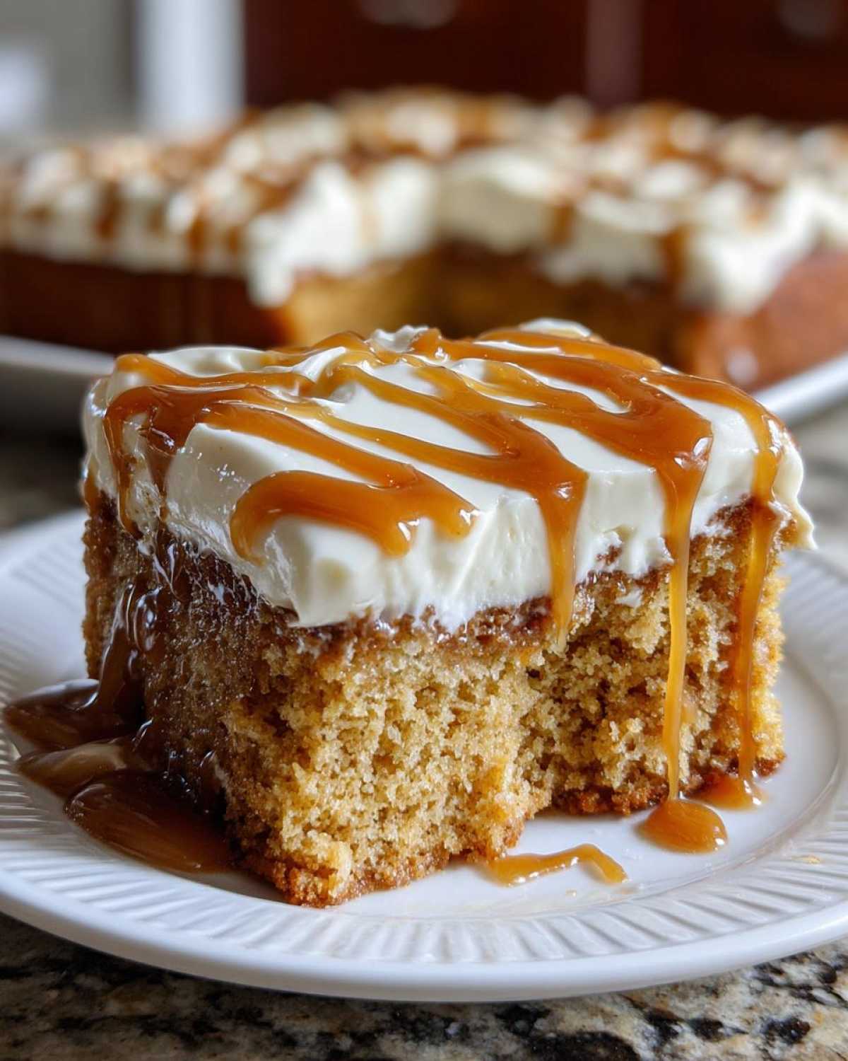 A moist slice of pumpkin poke cake topped with cream cheese frosting and drizzled heavily with caramel sauce.