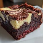 Close-up of a moist, dark red velvet cheesecake brownies square with a creamy cheesecake swirl on top.
