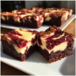 Two squares of rich red velvet cheesecake brownies with a marbled cream cheese swirl, cut and placed on a white plate.