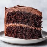 Close-up of a moist, dark slice of chocolate cake recipe with two layers and thick chocolate frosting.