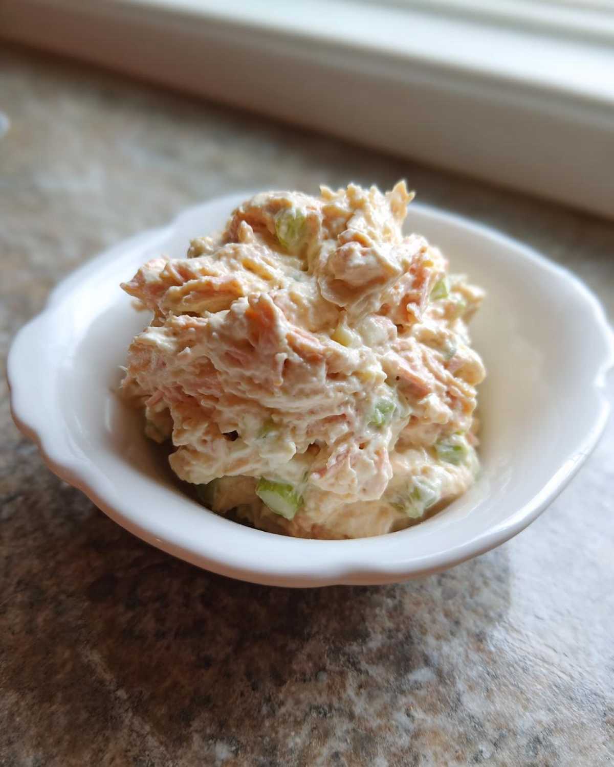 A small white bowl filled with creamy ham salad recipe, showing shredded ham and visible celery pieces.