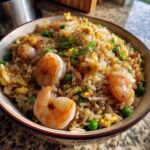 Close-up of a bowl filled with savory shrimp fried rice, featuring plump shrimp, scrambled egg, and green peas.