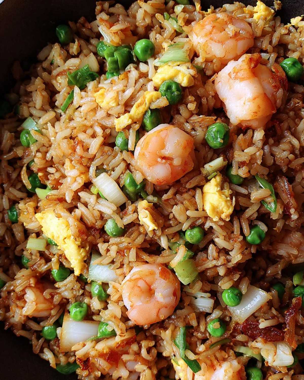 Close-up overhead shot of perfectly cooked shrimp fried rice featuring plump shrimp, green peas, scrambled egg, and onion pieces.