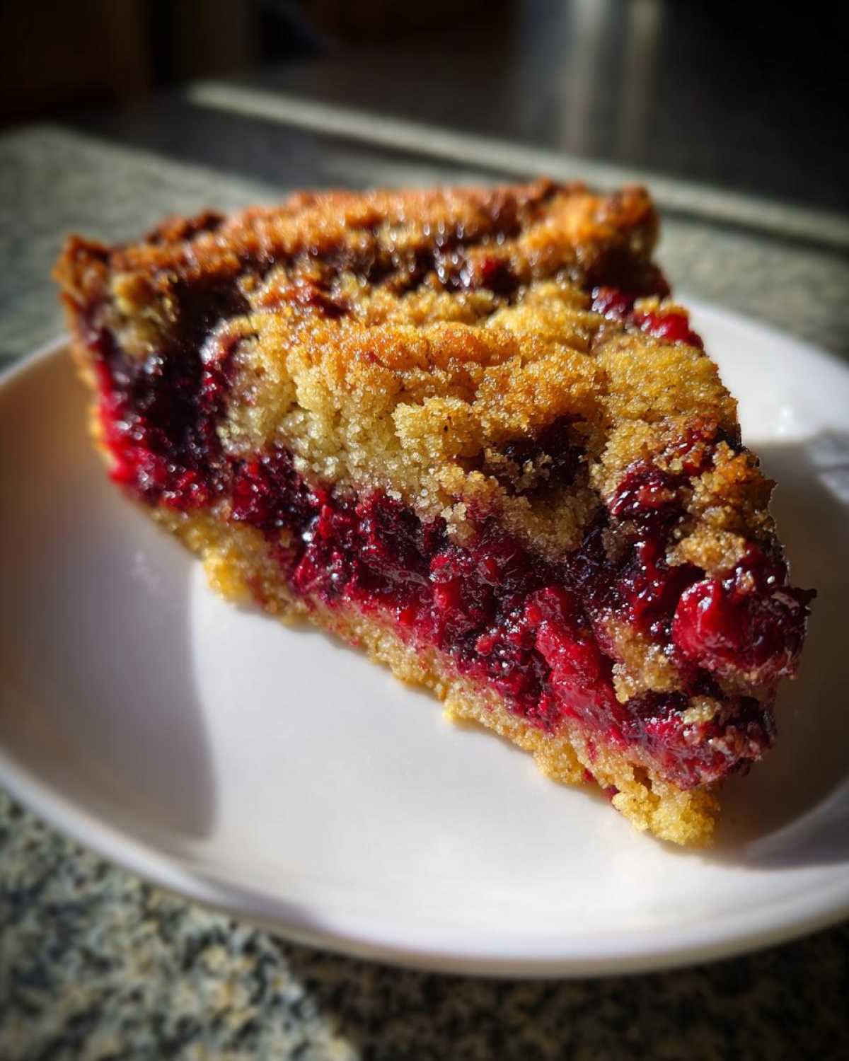 A close-up slice of Nantucket cranberry pie showing the bright red cranberry filling and golden crumb topping.