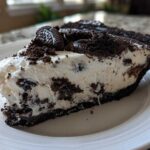 A generous slice of creamy, no-bake Oreo pie featuring a dark crust and white filling mixed with chocolate cookie pieces.