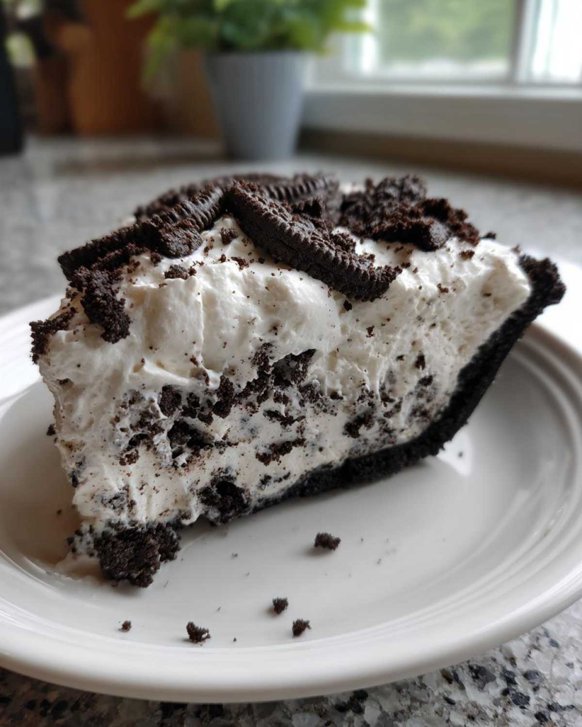 A generous slice of Oreo pie featuring a dark crust, creamy filling mixed with cookie pieces, and topped with whipped cream and mini Oreos.
