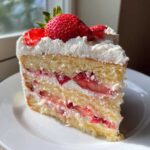 A moist slice of 3-layer strawberry cake with whipped cream frosting and fresh strawberries on top.