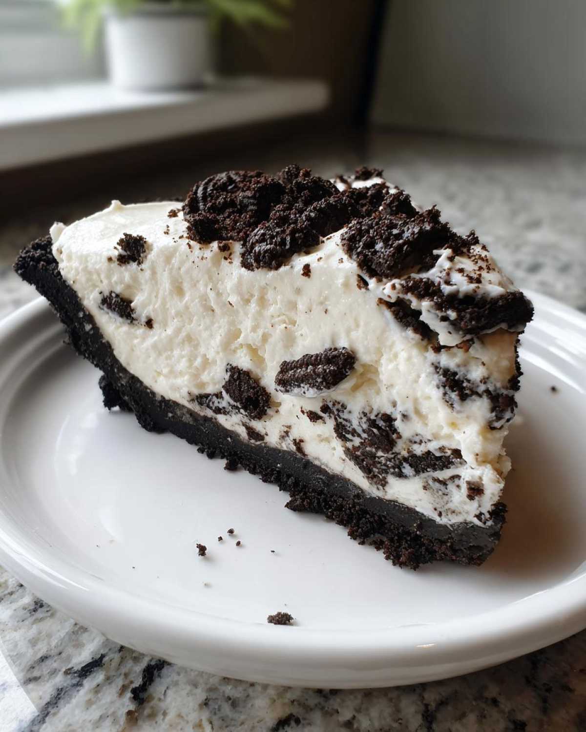A close-up of a generous slice of creamy Oreo pie with a dark chocolate crust and cookie chunks.
