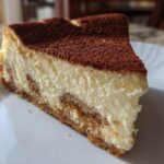 A close-up view of a perfect slice of tiramisu cheesecake, showing the creamy filling and cocoa powder topping.