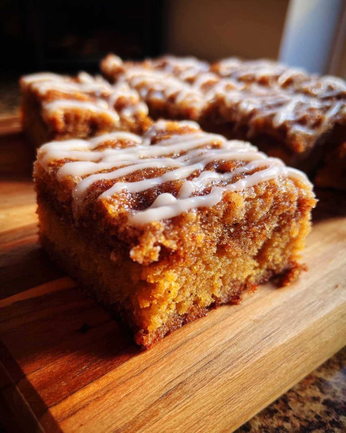 A close-up, warmly lit square of snickerdoodle blondies topped with a white cinnamon glaze drizzle.