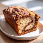 A close-up of a golden brown snickerdoodle zucchini bread loaf with a cinnamon swirl and sugary topping.